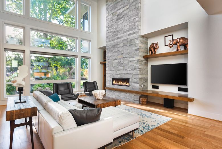 Bright modern living room with floor-to-ceiling windows, stone fireplace, white sofas, and wood floors