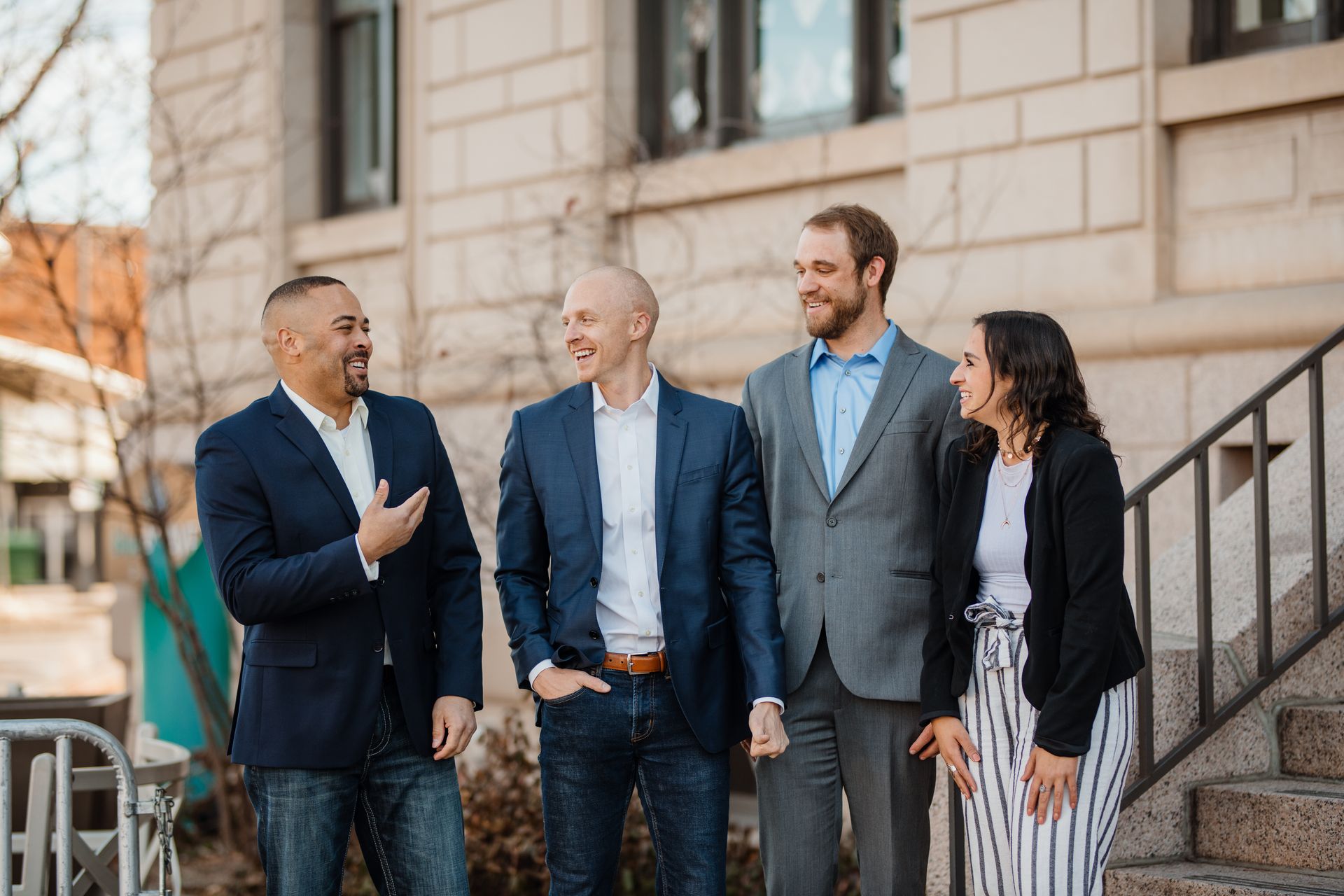 Four coworkers in business attire chatting outside a stone office building