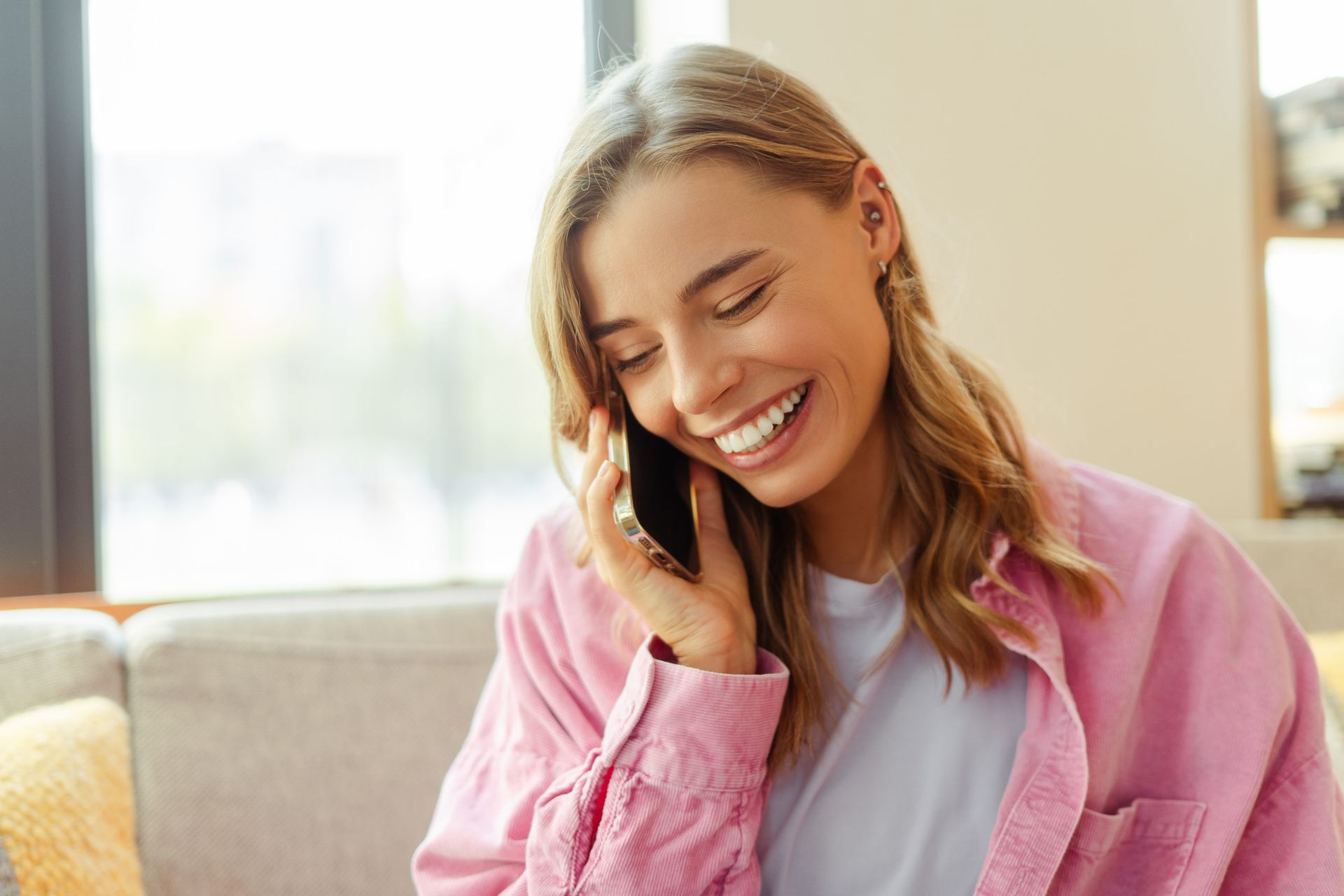 Smiling woman in a pink shirt talking on a phone on a couch
