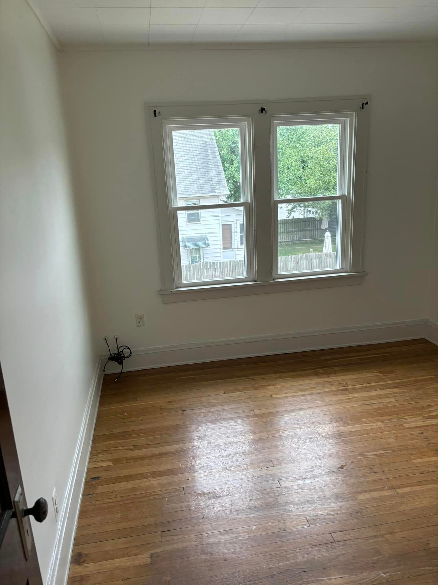 An empty room with hardwood floors and two windows.