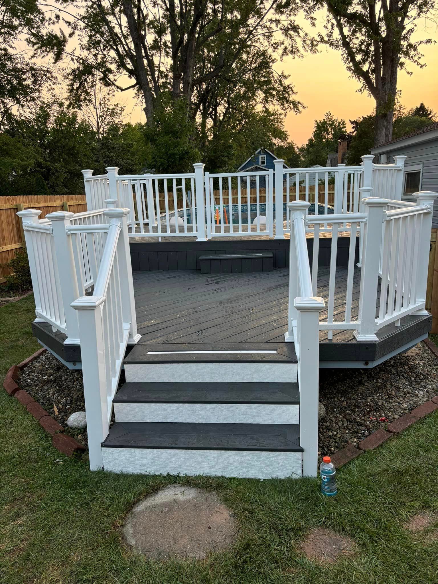 A deck with stairs and a white railing in a backyard.