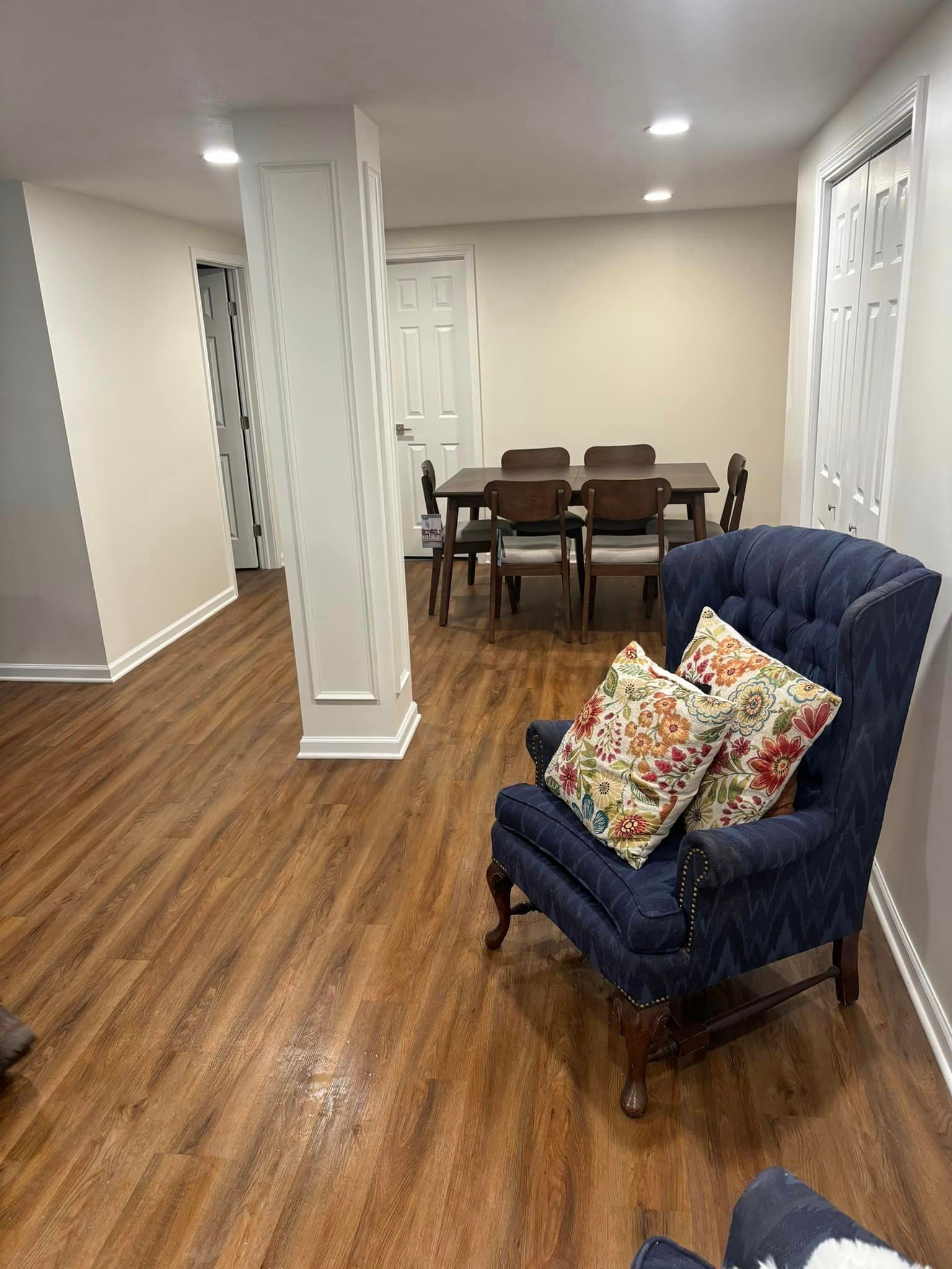 A living room with hardwood floors , a chair , a table and chairs.