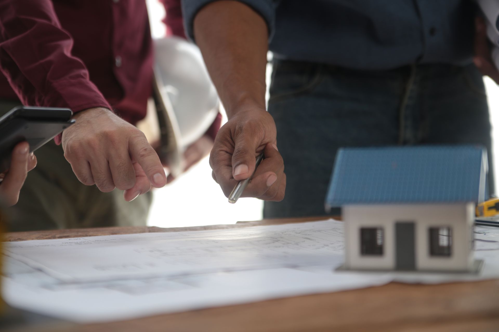 Construction team reviewing architectural blueprints and floor plans with hard hat and house model.