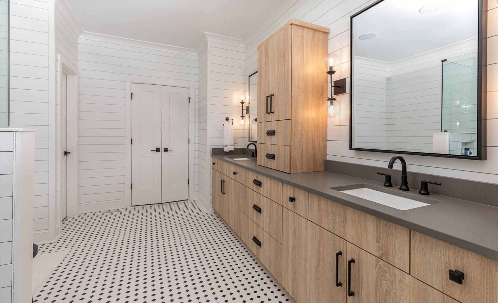 Modern bathroom with black-and-white patterned tile, wood vanities, and large mirror