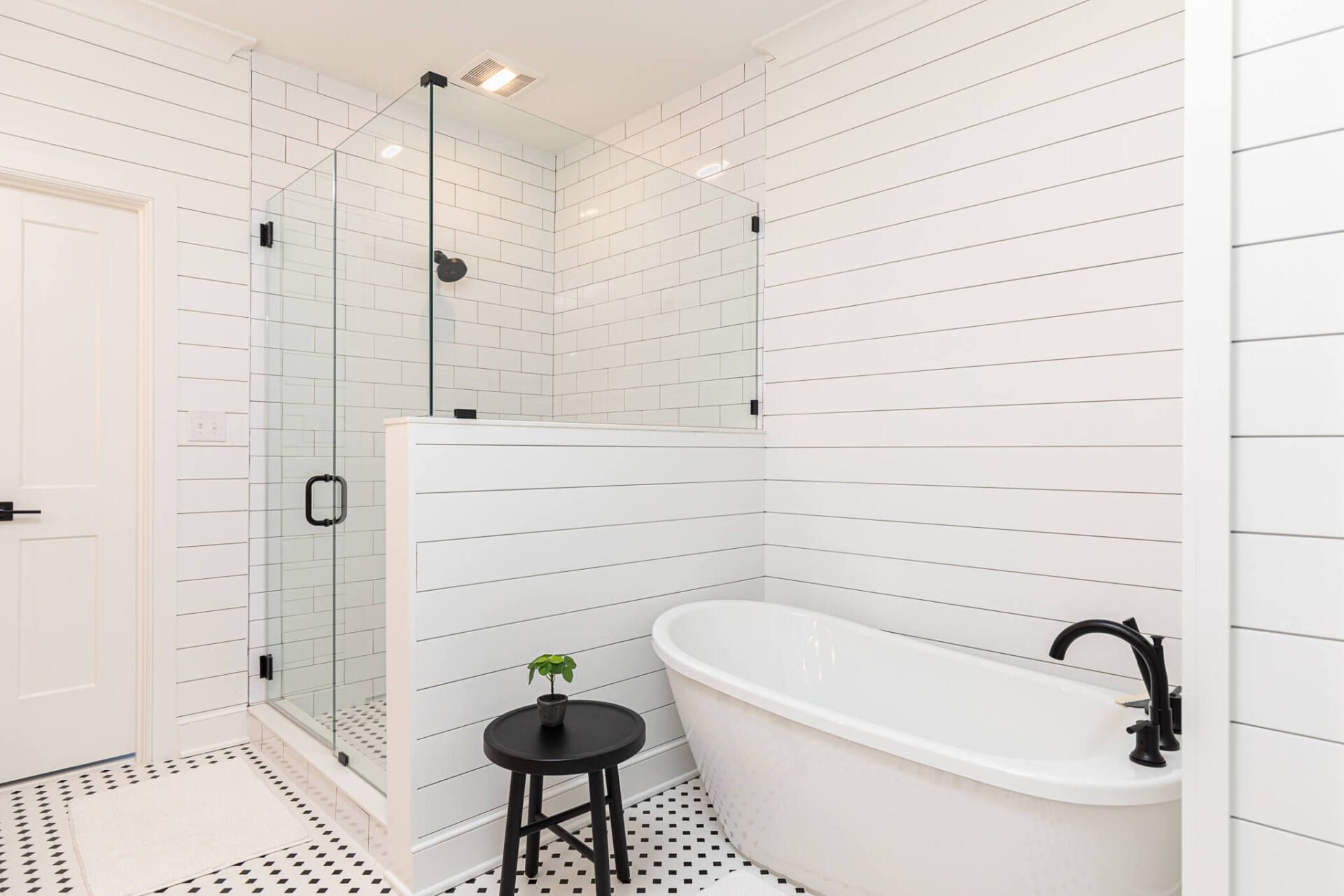 Bright white bathroom with glass shower, freestanding tub, and black fixtures
