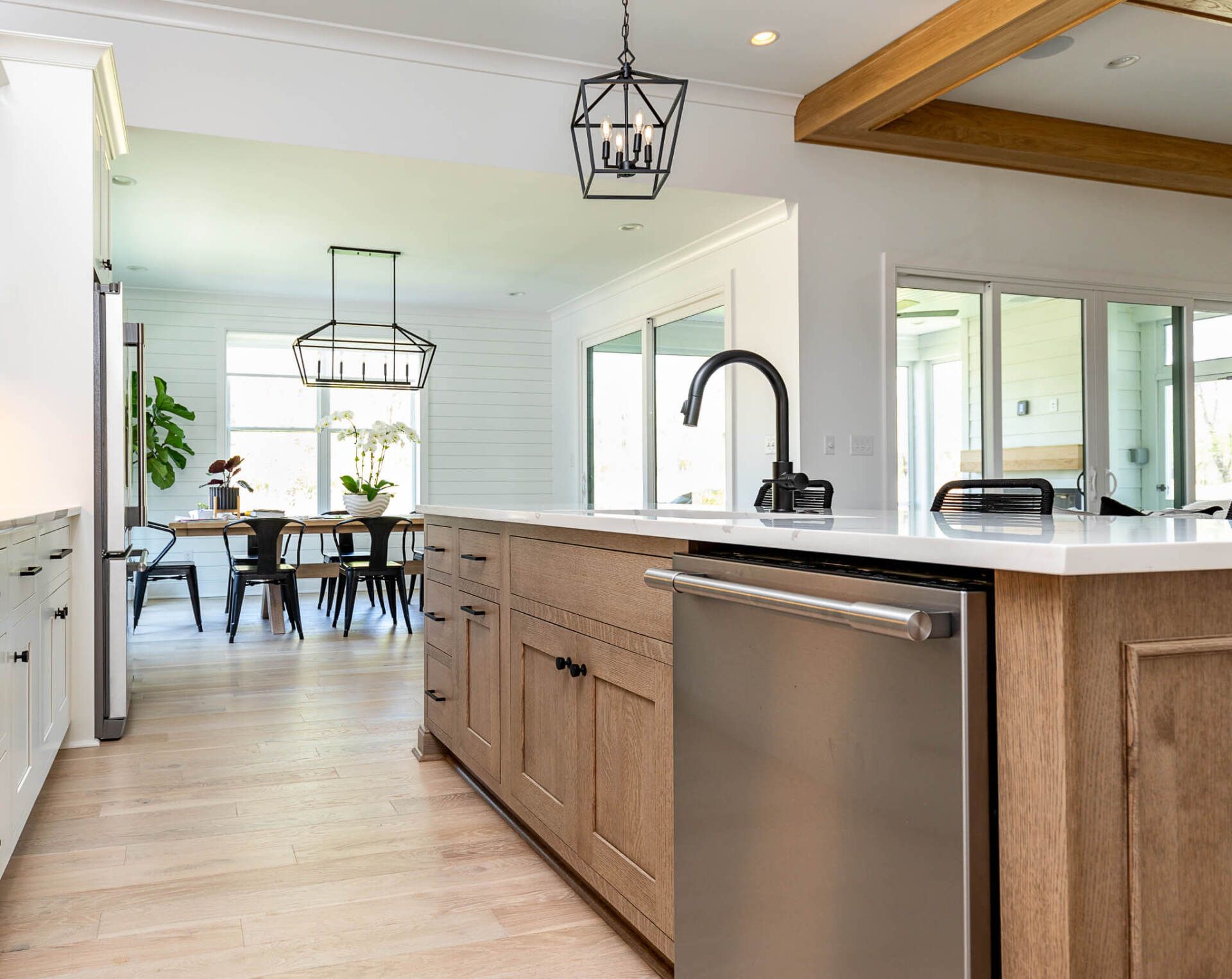 Bright modern kitchen with wood island, black fixtures, and dining area by windows
