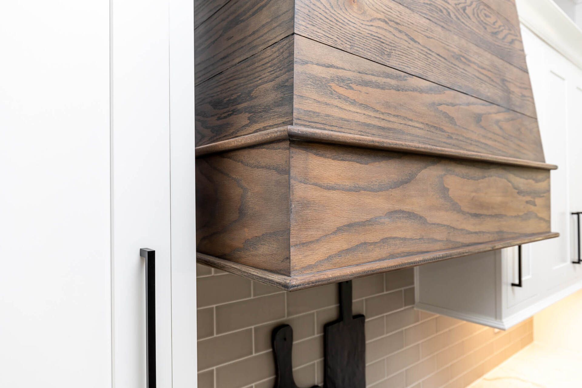 Modern wood range hood above a tiled kitchen backsplash with white cabinets