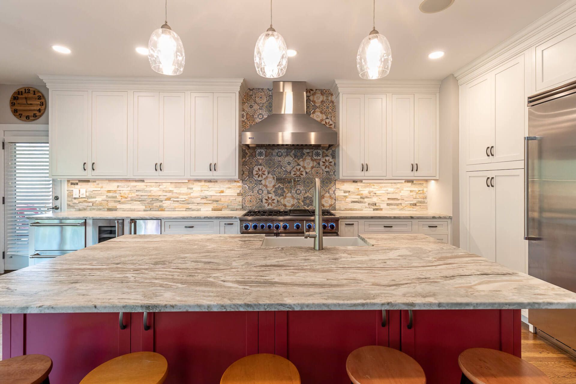 Modern white kitchen with marble island, pendant lights, stainless fridge, and red bar stools