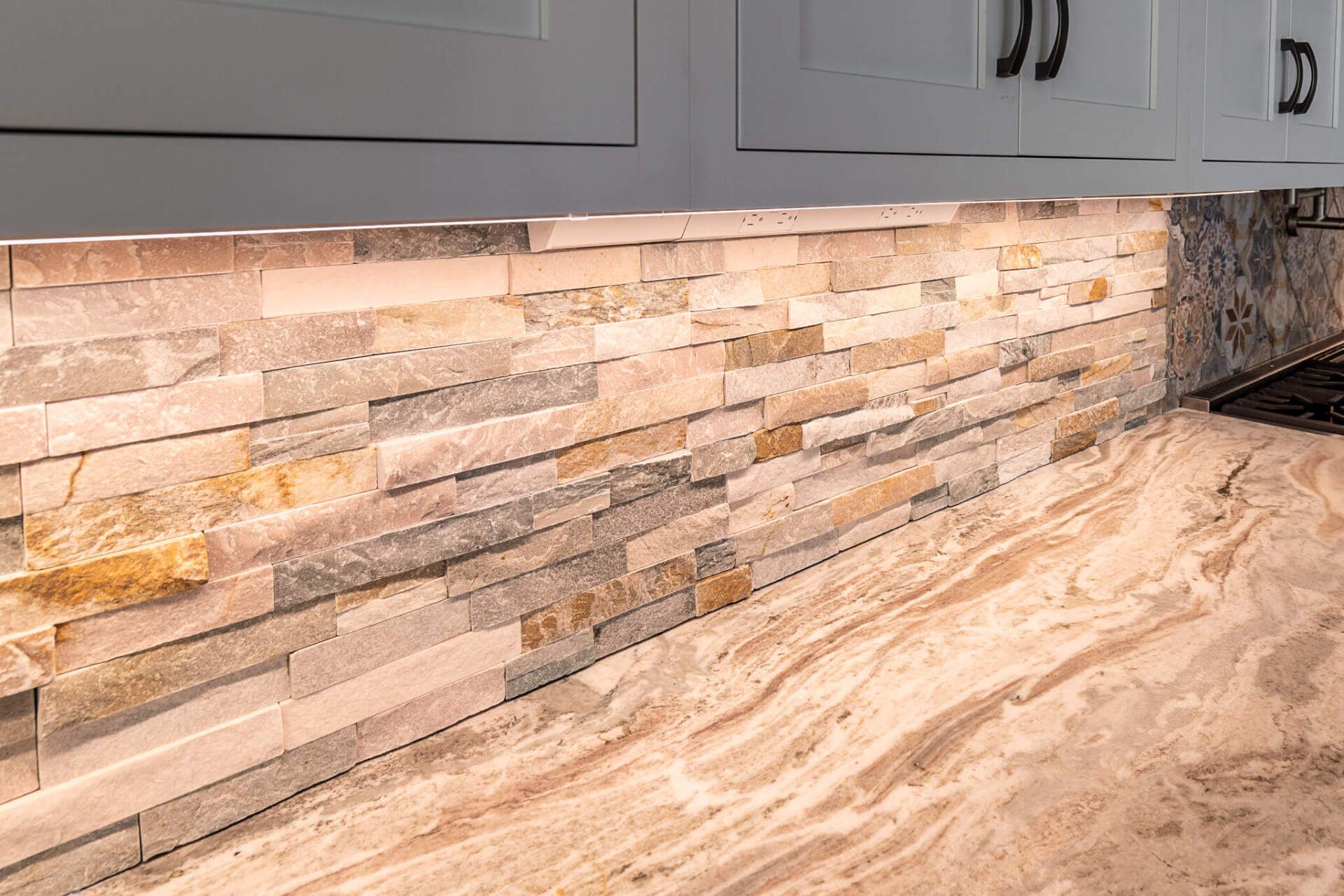 Stone tile backsplash with gray cabinets and a beige marble kitchen countertop