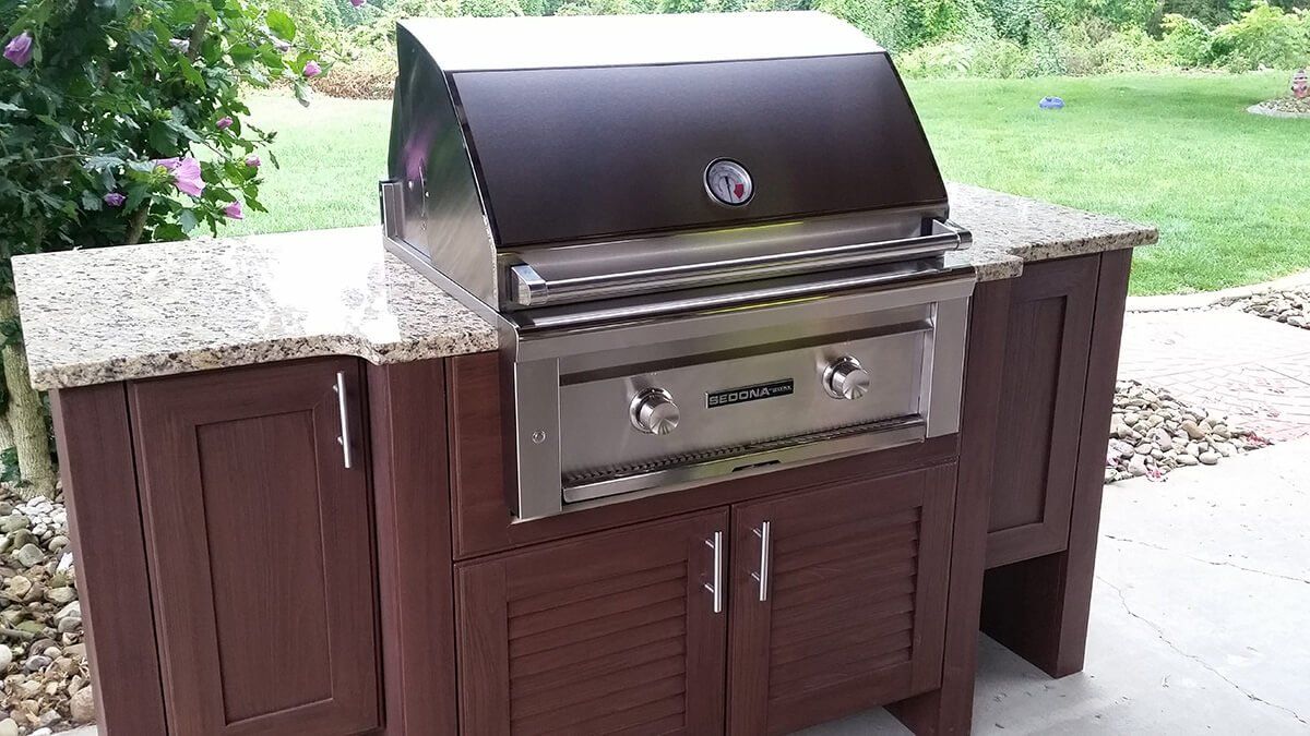 Outdoor stainless steel grill built into a brown cabinet on a patio with a speckled countertop