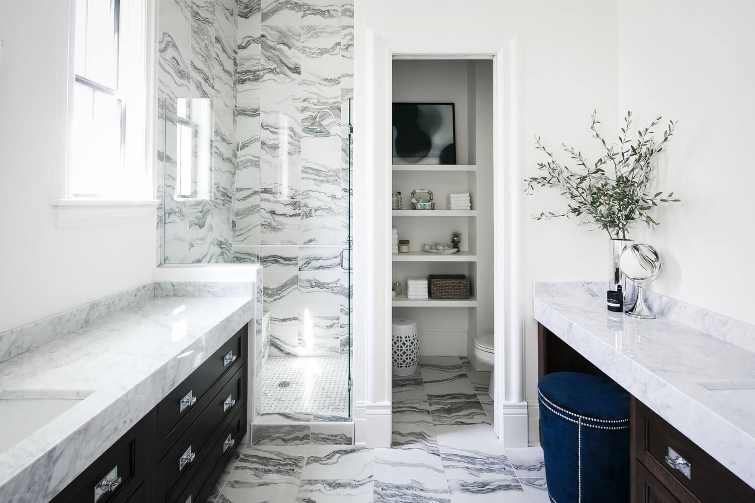 Bright marble bathroom with black vanity, walk-in shower, and open shelving