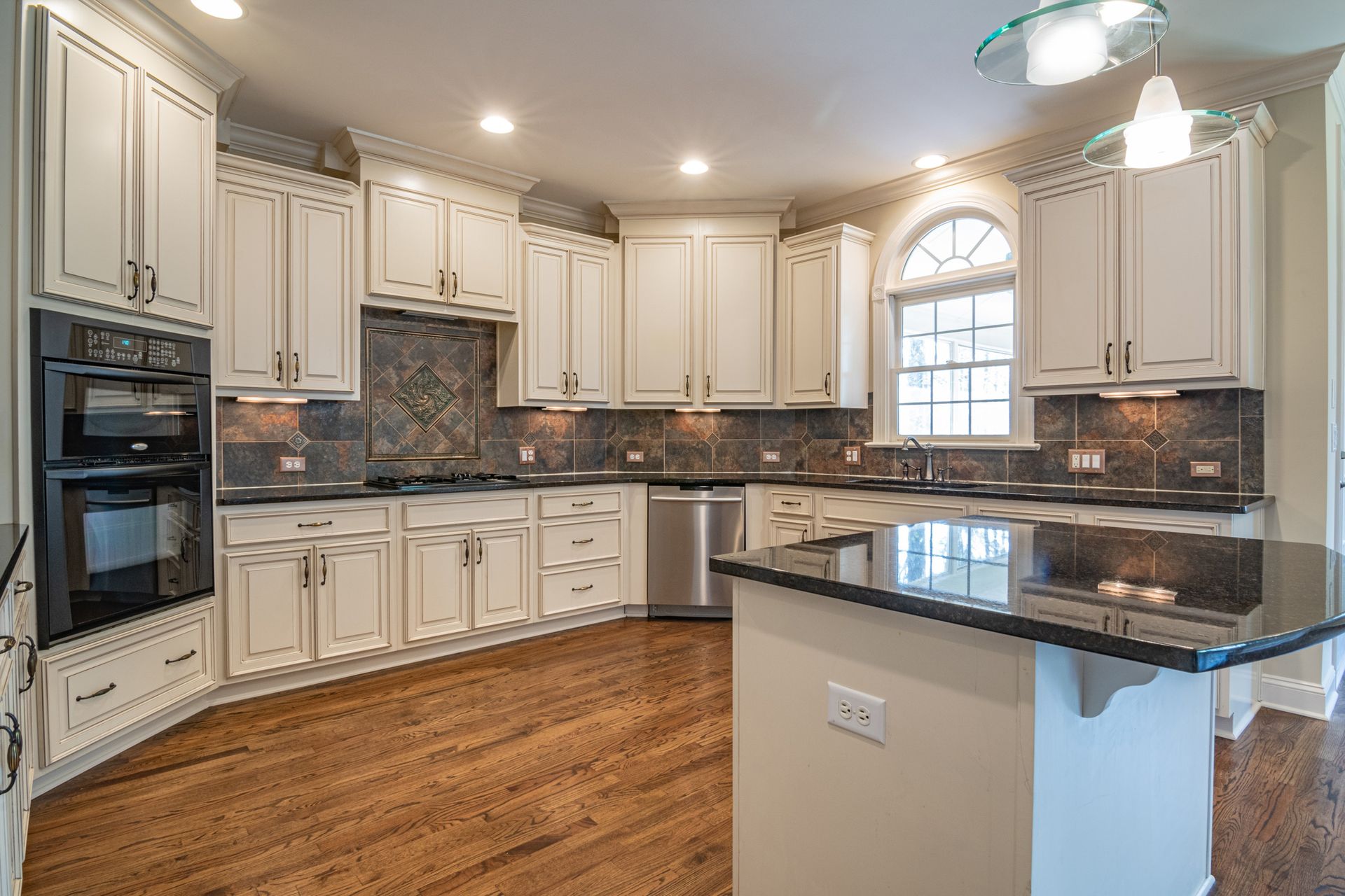 Bright modern kitchen with white cabinets, dark granite counters, and hardwood floors