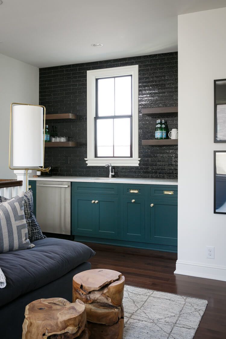 Modern living room with teal built-in cabinets, dark tile wall, and wood stump coffee tables