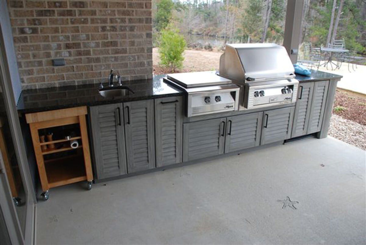 Outdoor patio with built-in black cabinets, sink, and stainless steel grill beside a brick wall.