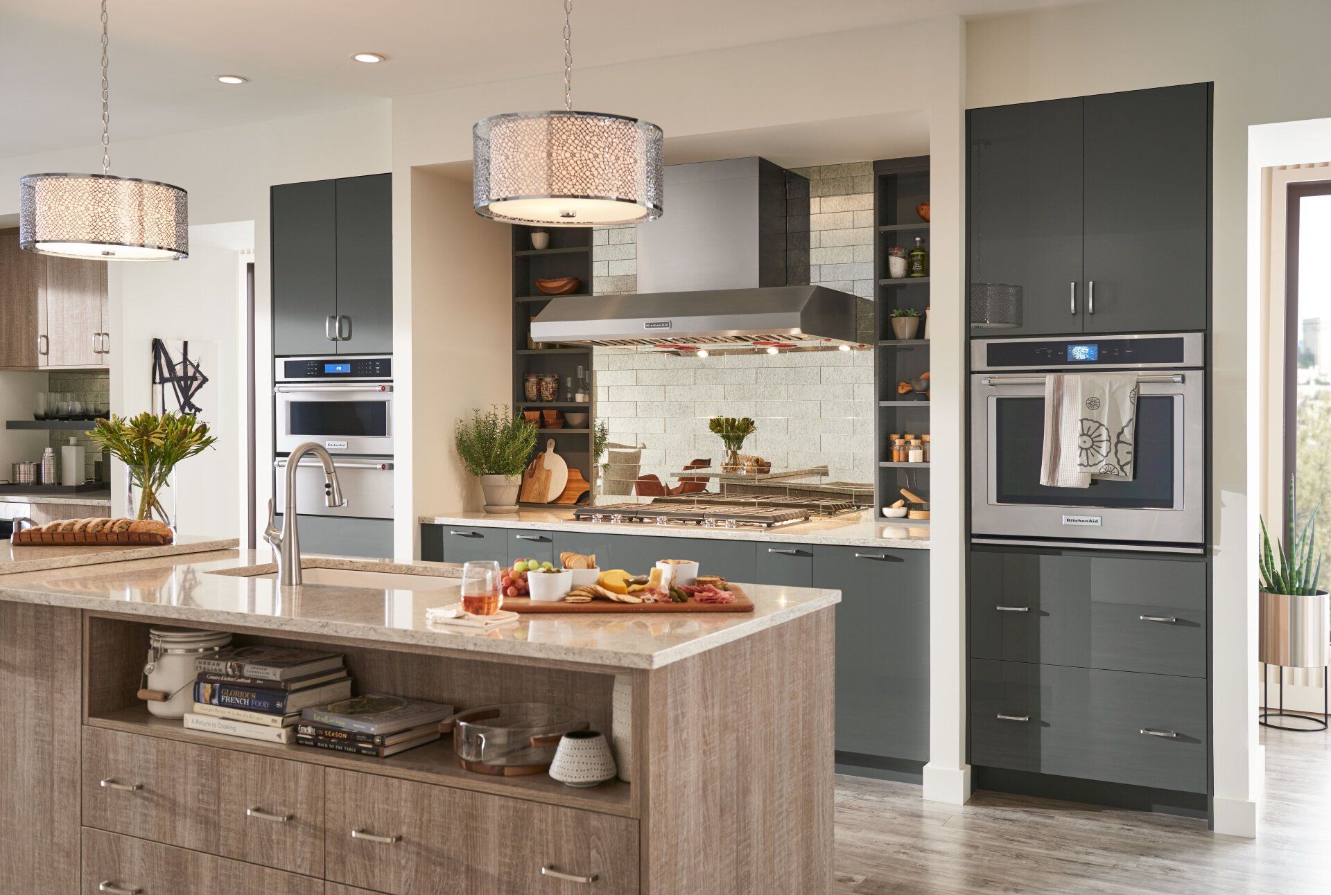Modern kitchen with island, built-in ovens, pendant lights, and a dining table with fruit and pastries