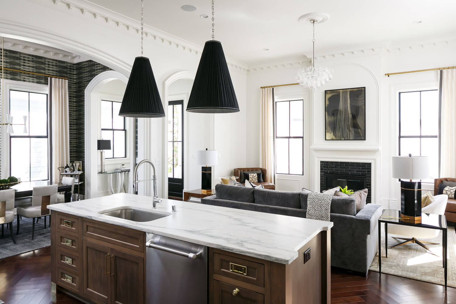 Bright open kitchen and living room with marble island, black pendant lights, gray sofa, and fireplace