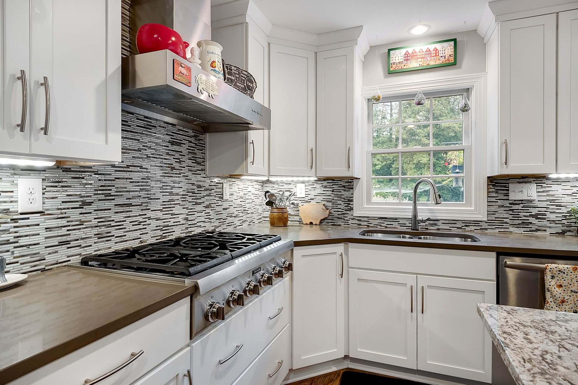 Bright white kitchen with mosaic tile backsplash, stainless stove, and window over the sink