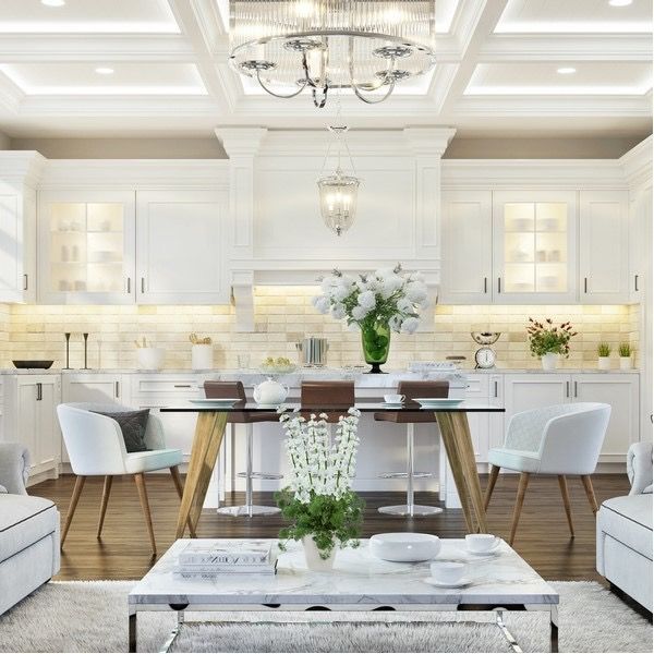 Elegant white dining room with chandelier, wood table, and vase of flowers on a marble coffee table