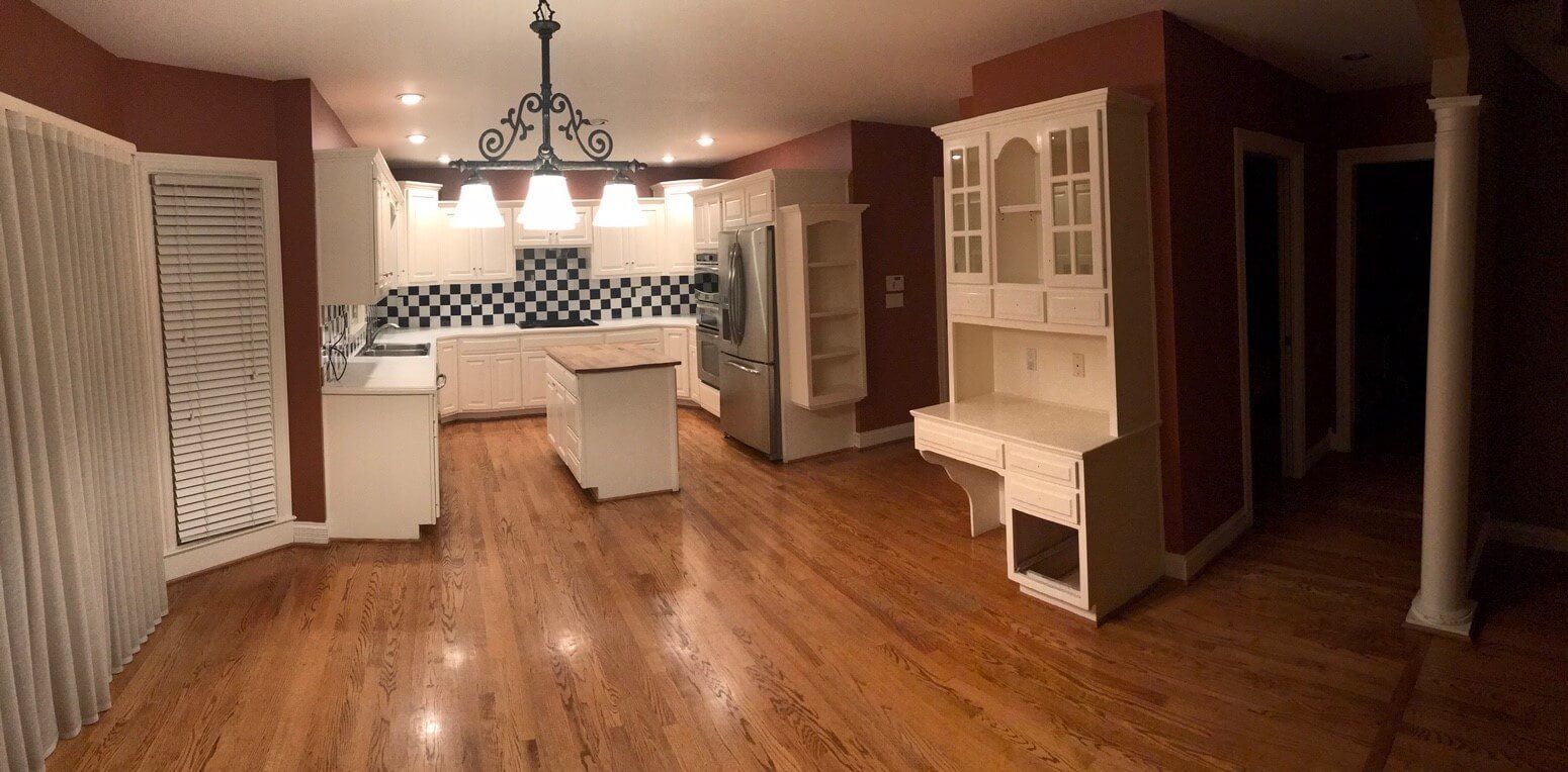 Empty kitchen with wood floors, white cabinets, and hanging light fixtures under warm lighting