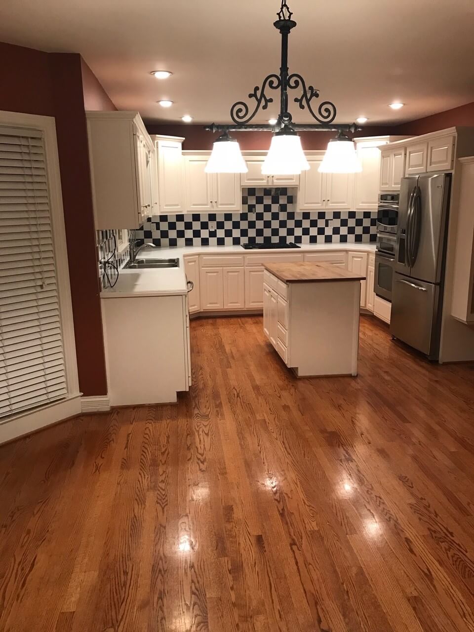 Spacious kitchen with white cabinets, stainless steel appliances, a central island, and warm wood floors.