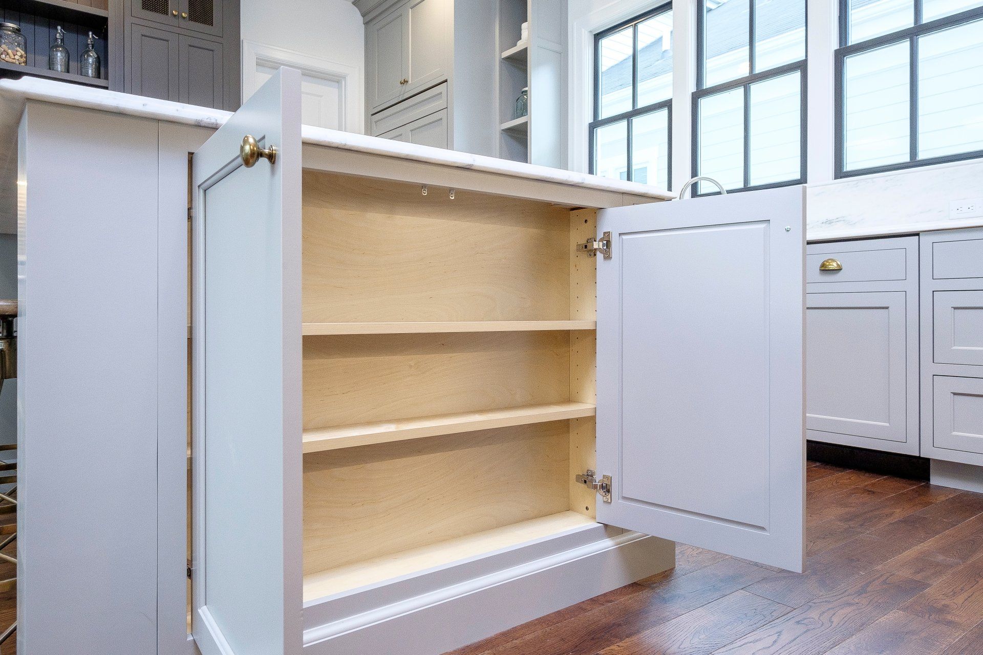 White kitchen cabinet with open shelves and a door, in a bright room with wood floors.