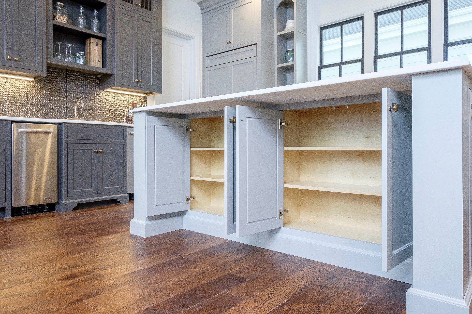 Open kitchen island cabinets in a modern kitchen with wood floors and gray cabinetry