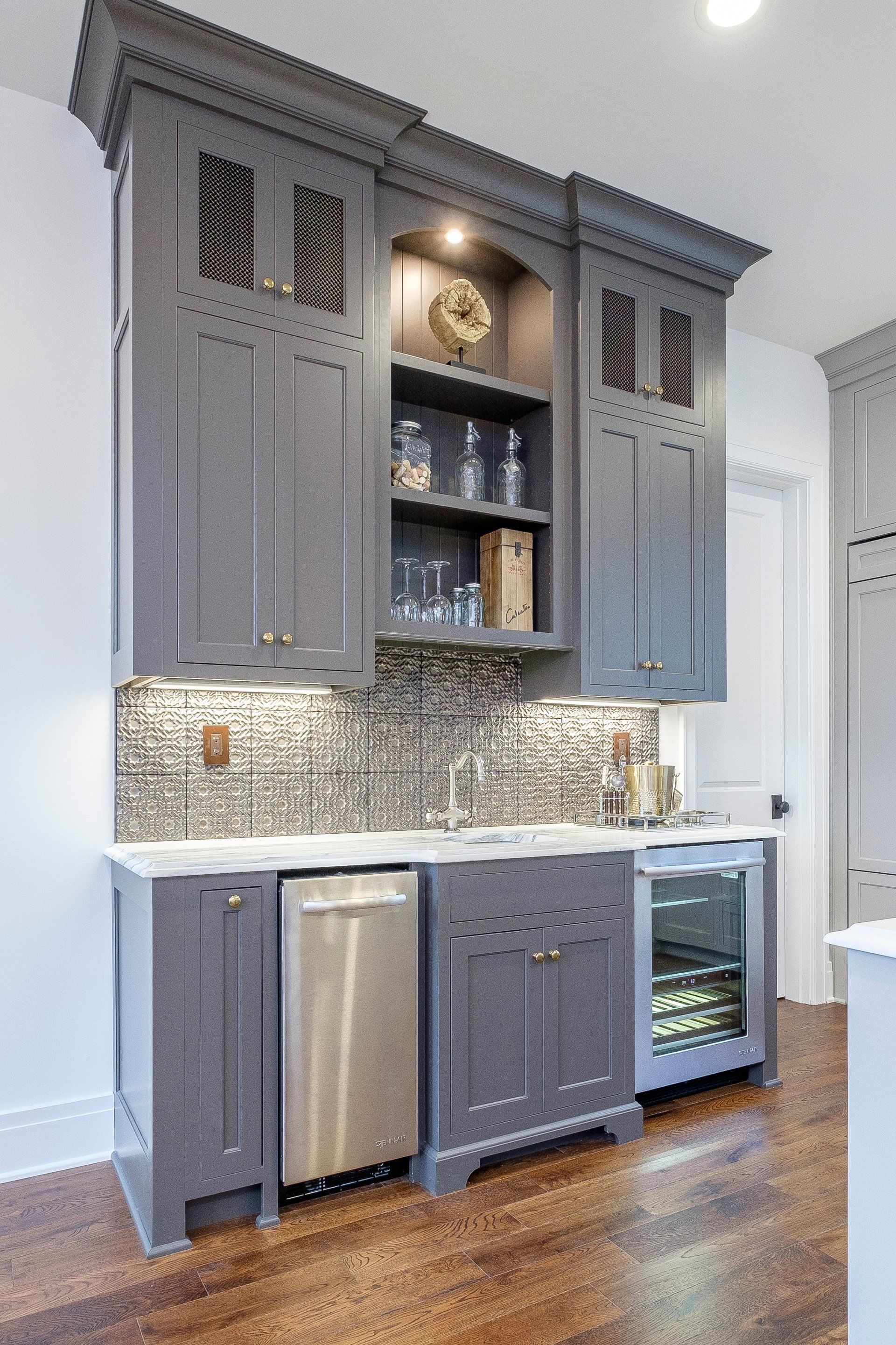 Gray kitchen cabinets with mosaic backsplash, stainless dishwasher, and wood floors under recessed lighting