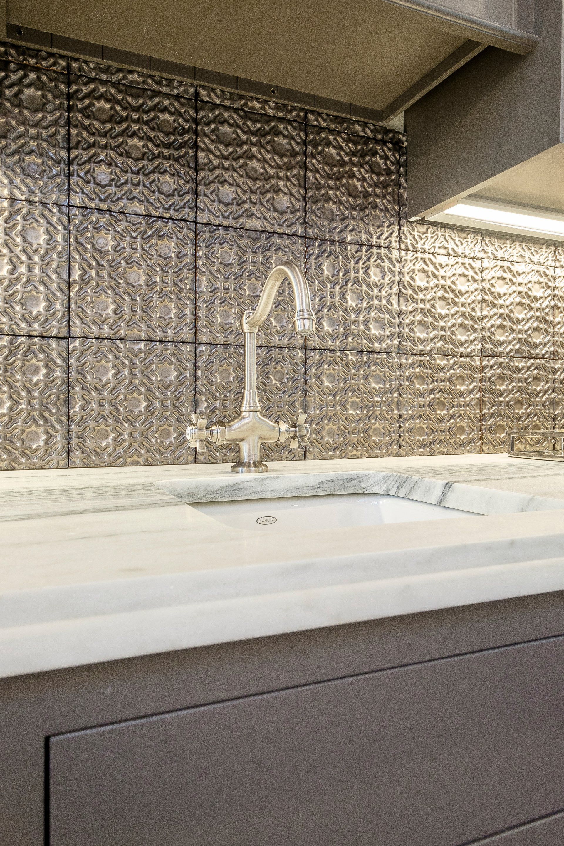 Modern kitchen sink with white countertop, chrome faucet, and textured gray tile backsplash