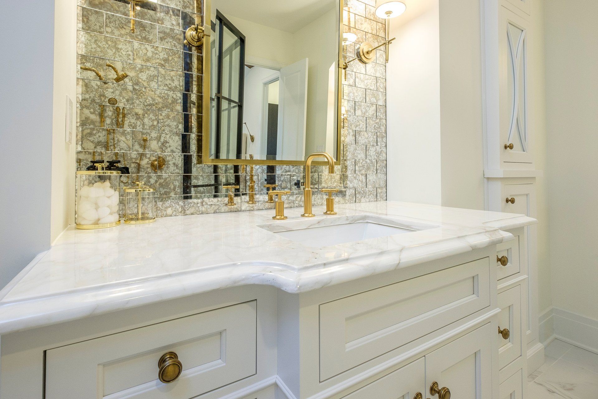 Elegant white marble bathroom vanity with gold faucets and a large mirror