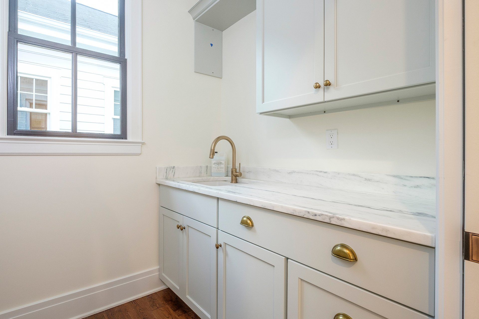 White built-in laundry room with marble counter, brass faucet, sink, cabinets, and window light