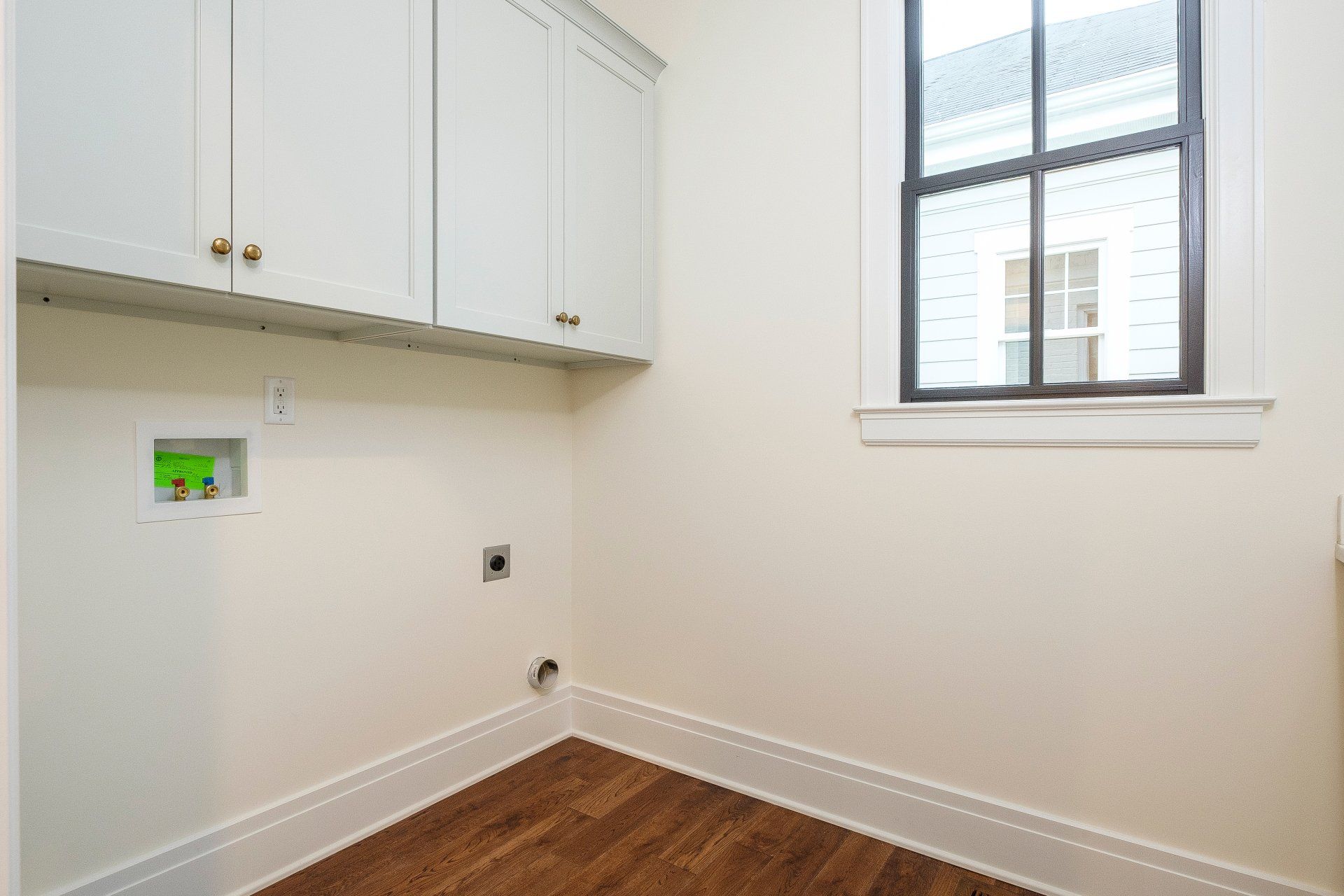 Empty laundry room with white cabinets, hookups, and a window over wood-look flooring