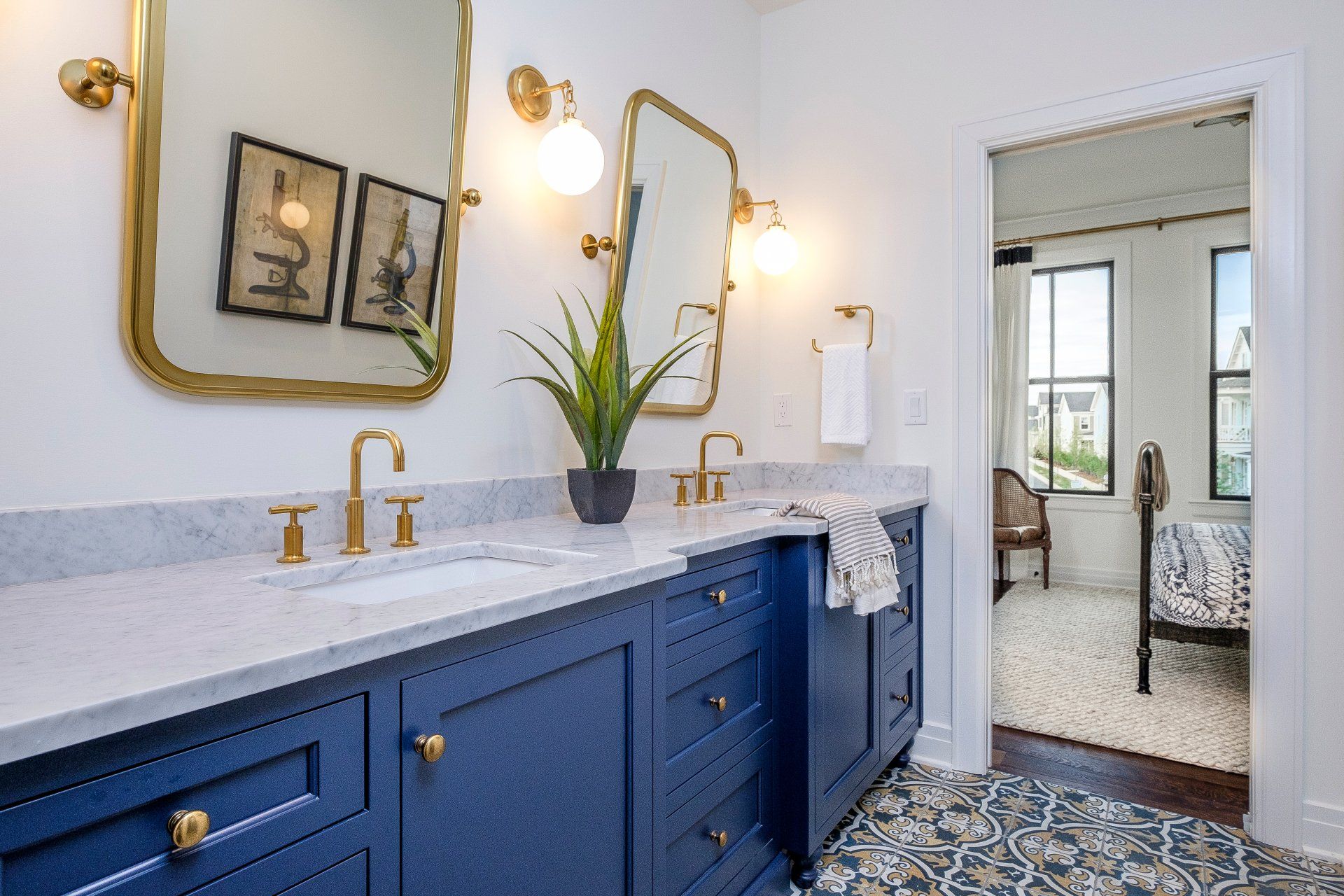 Blue bathroom vanity with gold fixtures, white countertop, mirrors, and patterned floor tiles