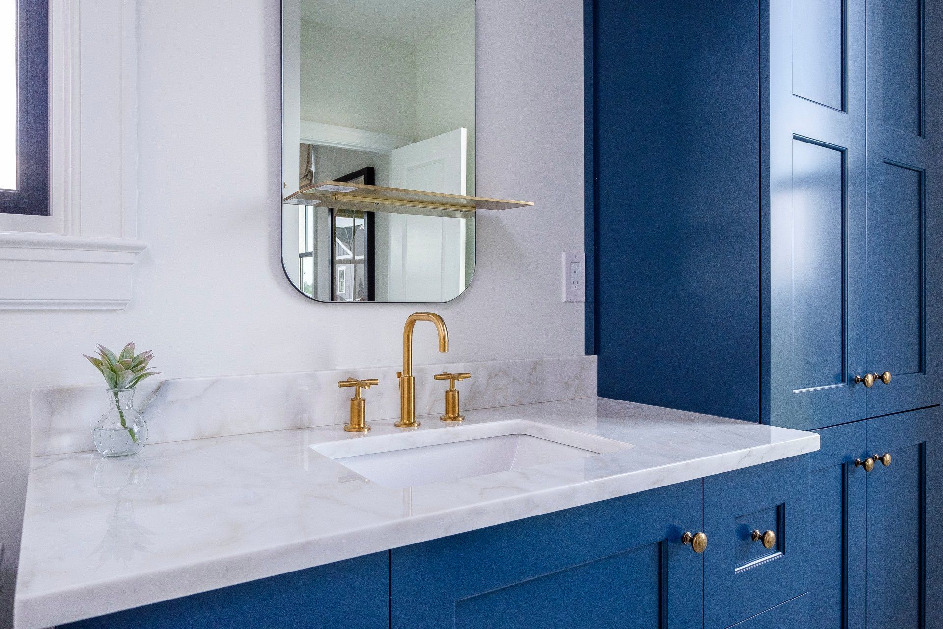Blue bathroom vanity with white countertop, gold faucet, mirror, and built-in cabinets