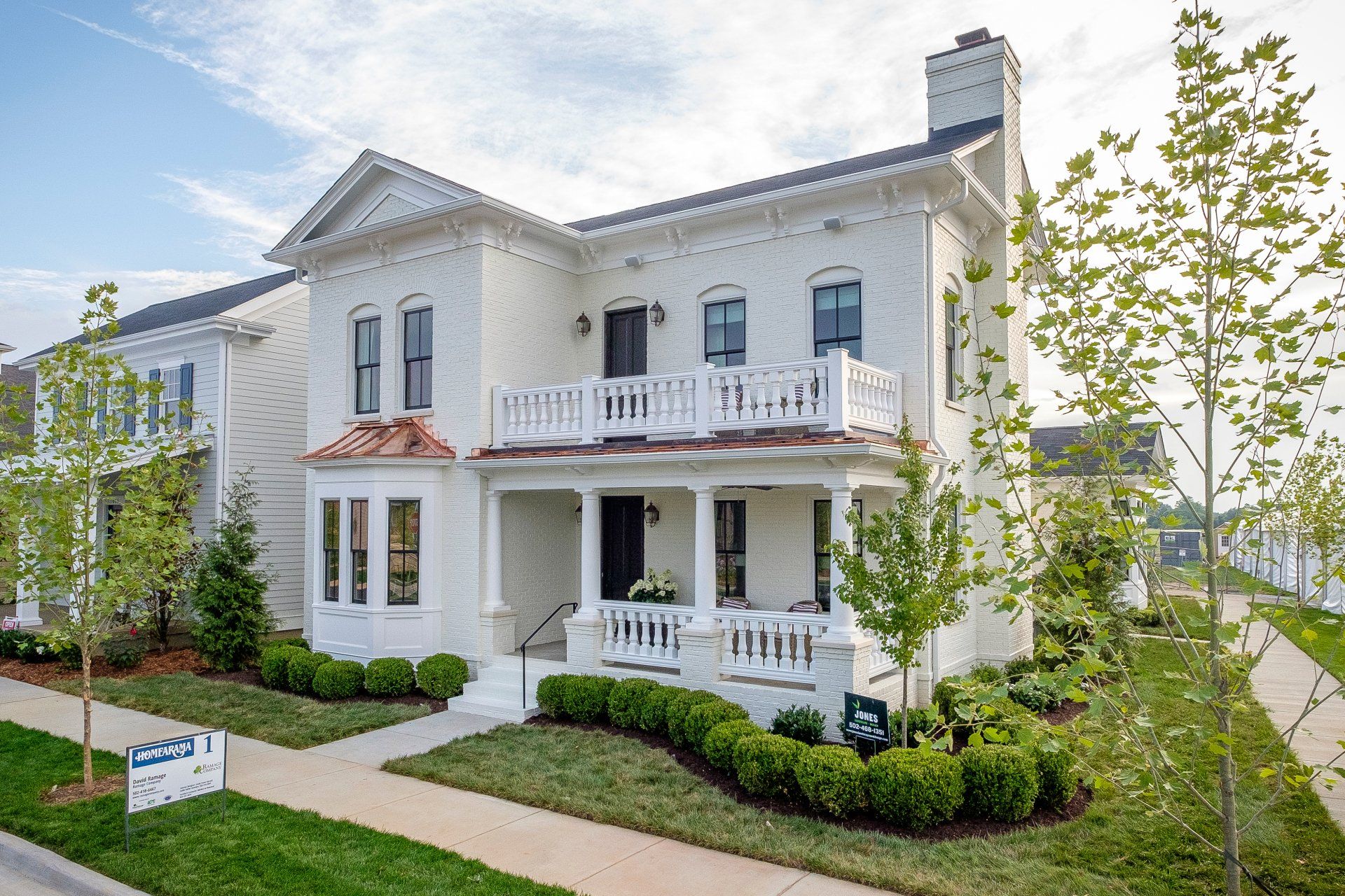 White two-story house with balcony, porch, and landscaped front yard under a blue sky