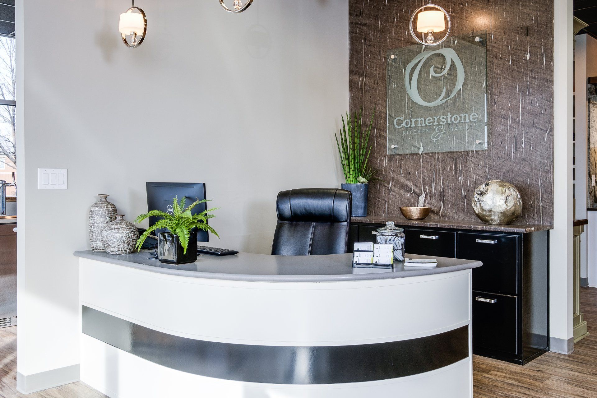 Modern office reception desk with black chairs, plants, and a wood-paneled wall logo