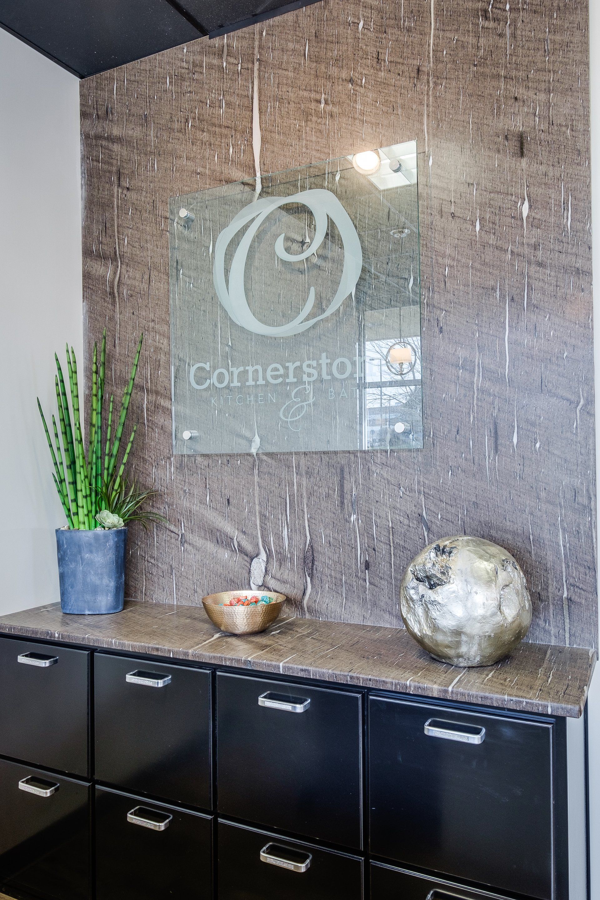 Modern office lobby with black cabinets, a potted plant, and a decorative logo wall sign