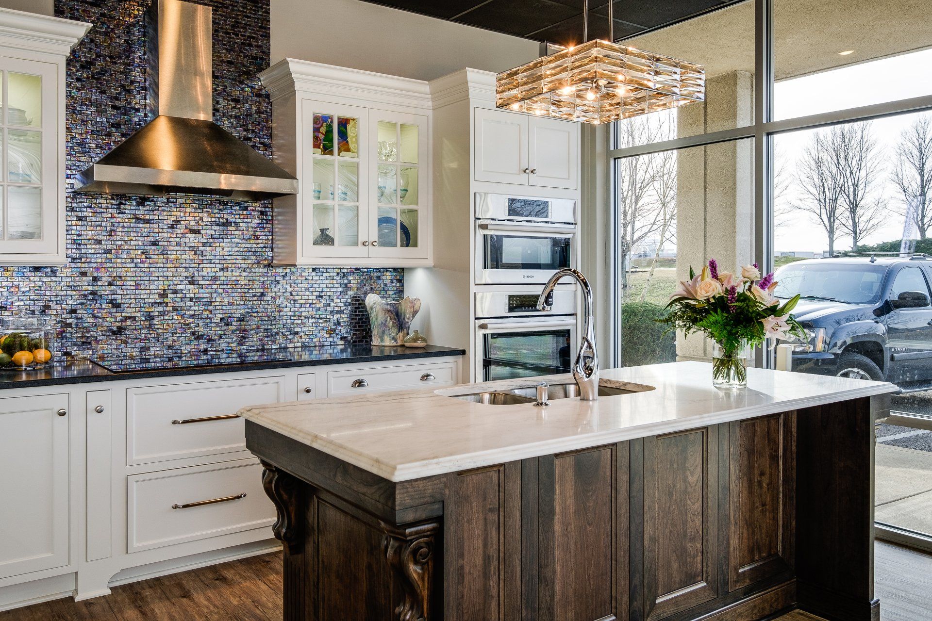 Bright modern kitchen with white cabinets, dark island, patterned backsplash, and large windows overlooking snow.