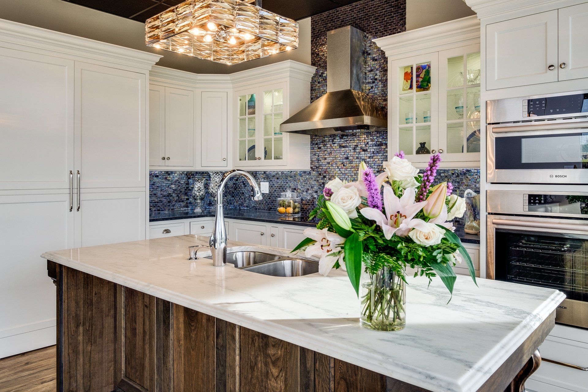 Modern white kitchen with marble island, pendant lights, and a vase of fresh flowers