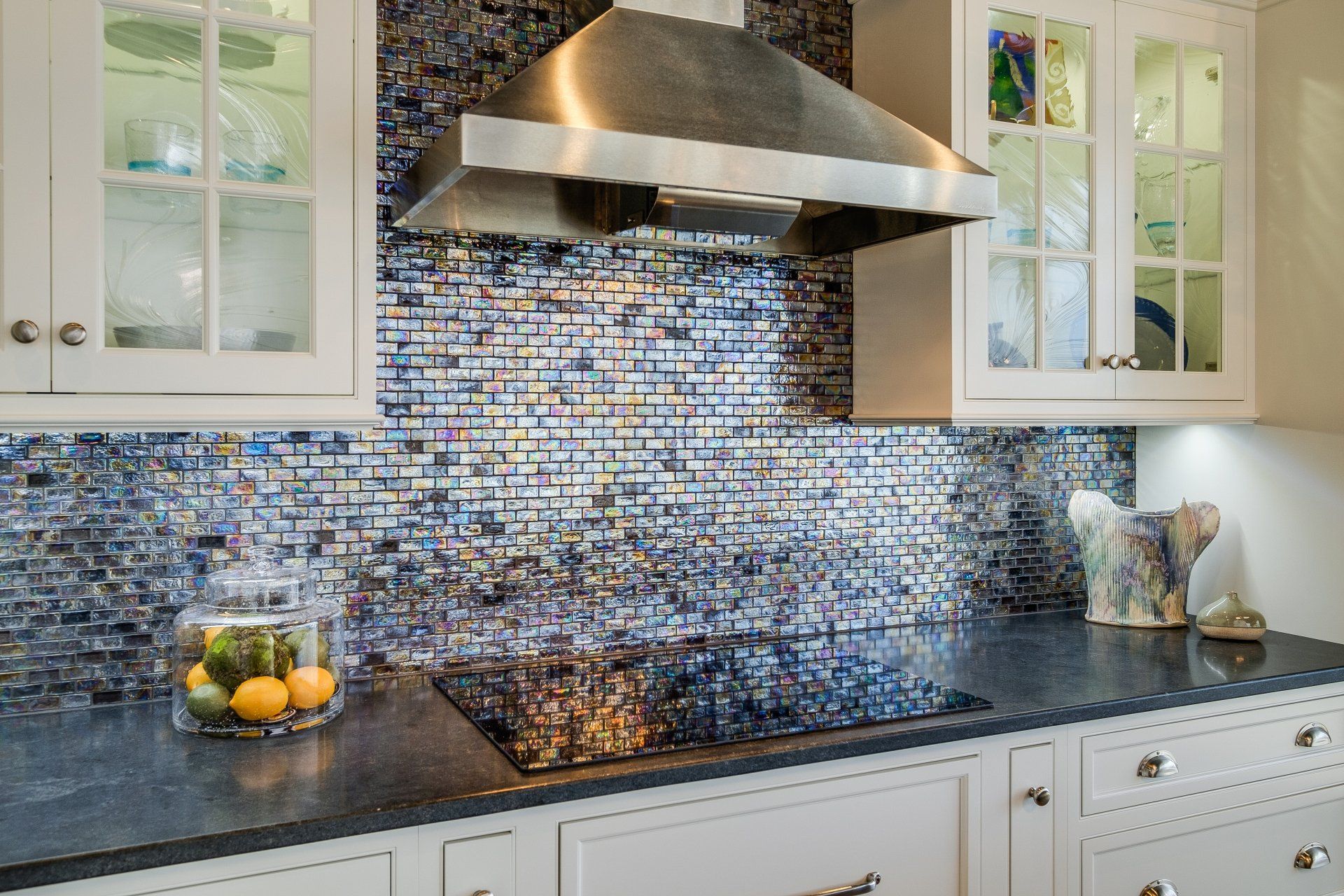 Modern kitchen with stainless hood, blue mosaic backsplash, black countertop, and white cabinets