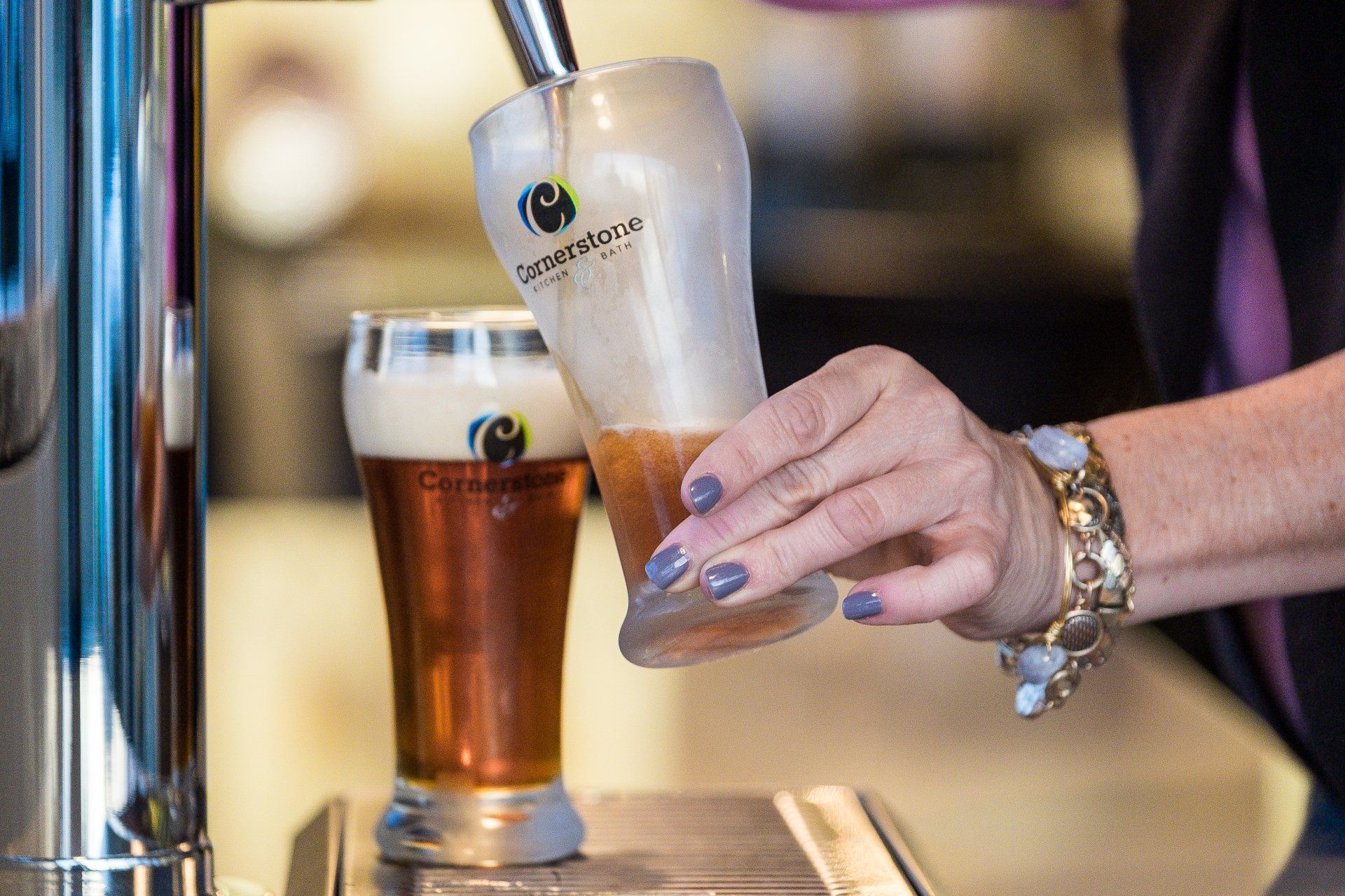 Hand pouring beer into a tilted pint glass beside a filled beer on a bar counter
