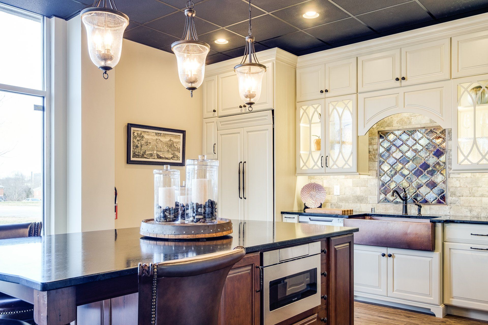 Bright kitchen with white cabinets, dark island, hanging pendant lights, and a built-in wine cooler.