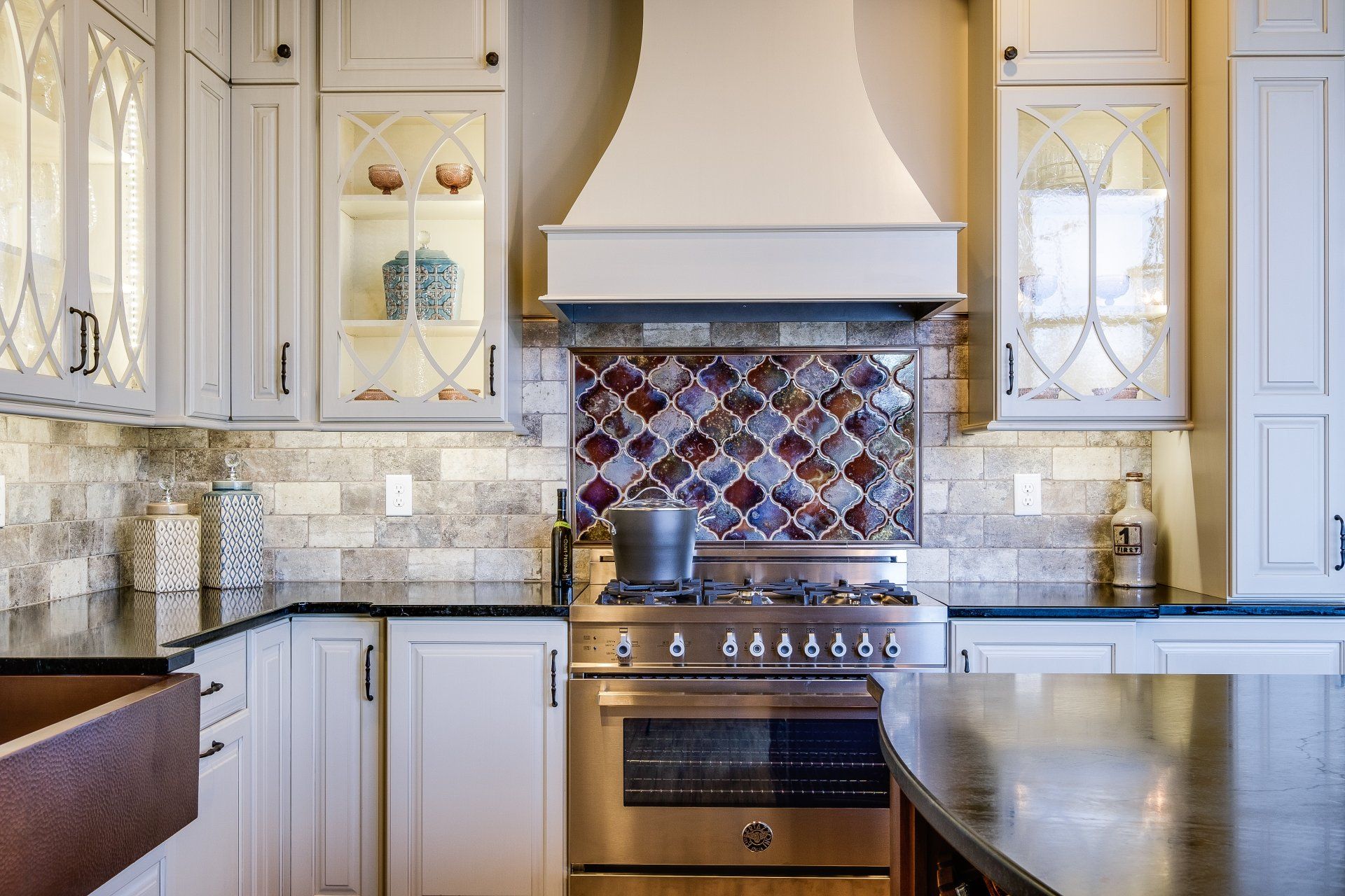 Bright kitchen with white cabinets, mosaic backsplash, stainless range, and dark countertops