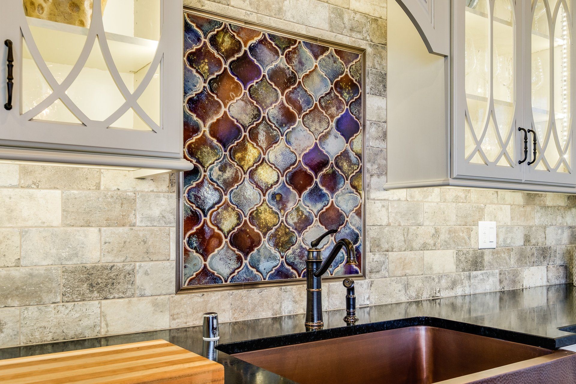 Kitchen sink with black faucet, stone backsplash, and decorative mosaic tile panel