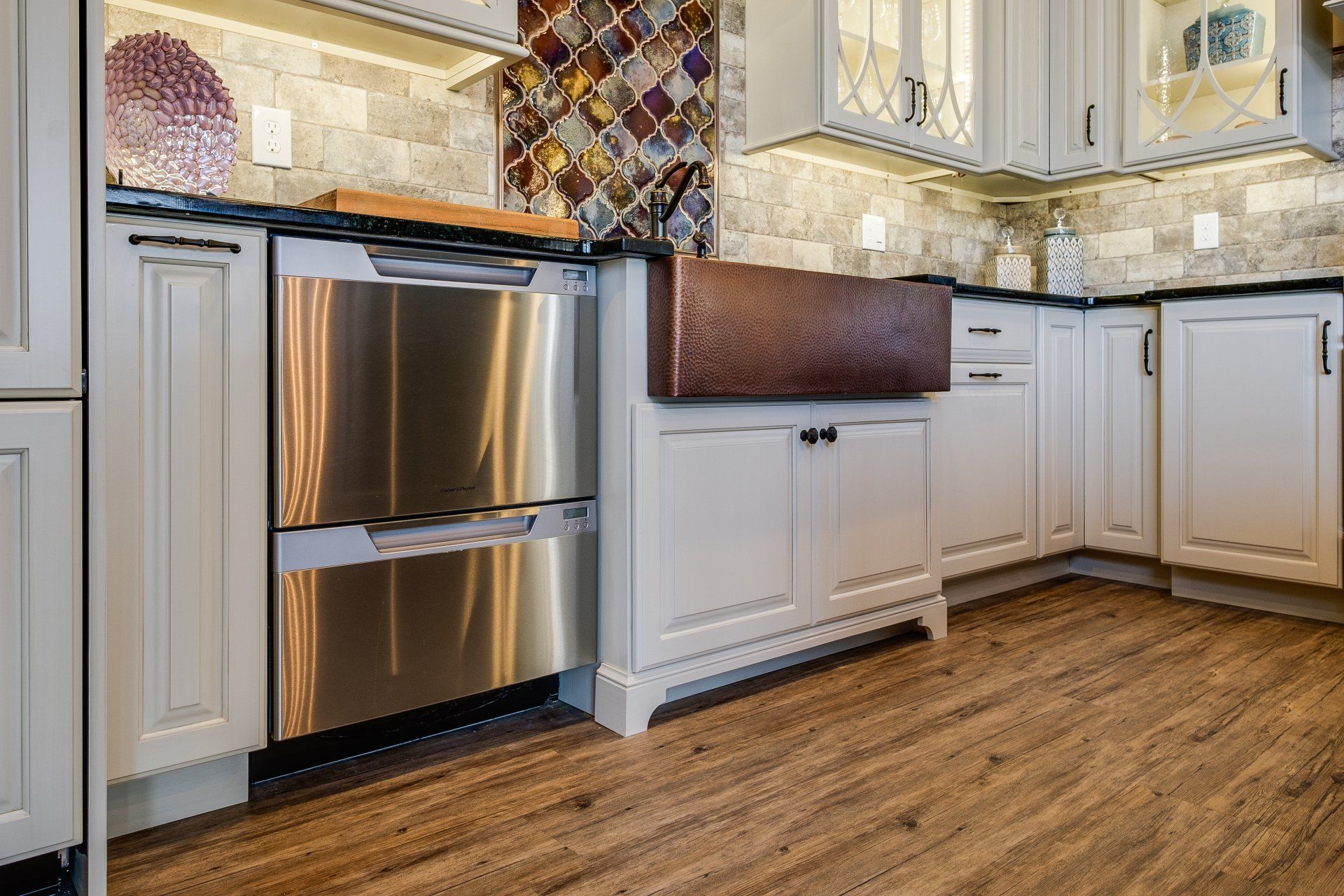 Modern kitchen with stainless steel refrigerator, white cabinets, beige backsplash, and wood flooring