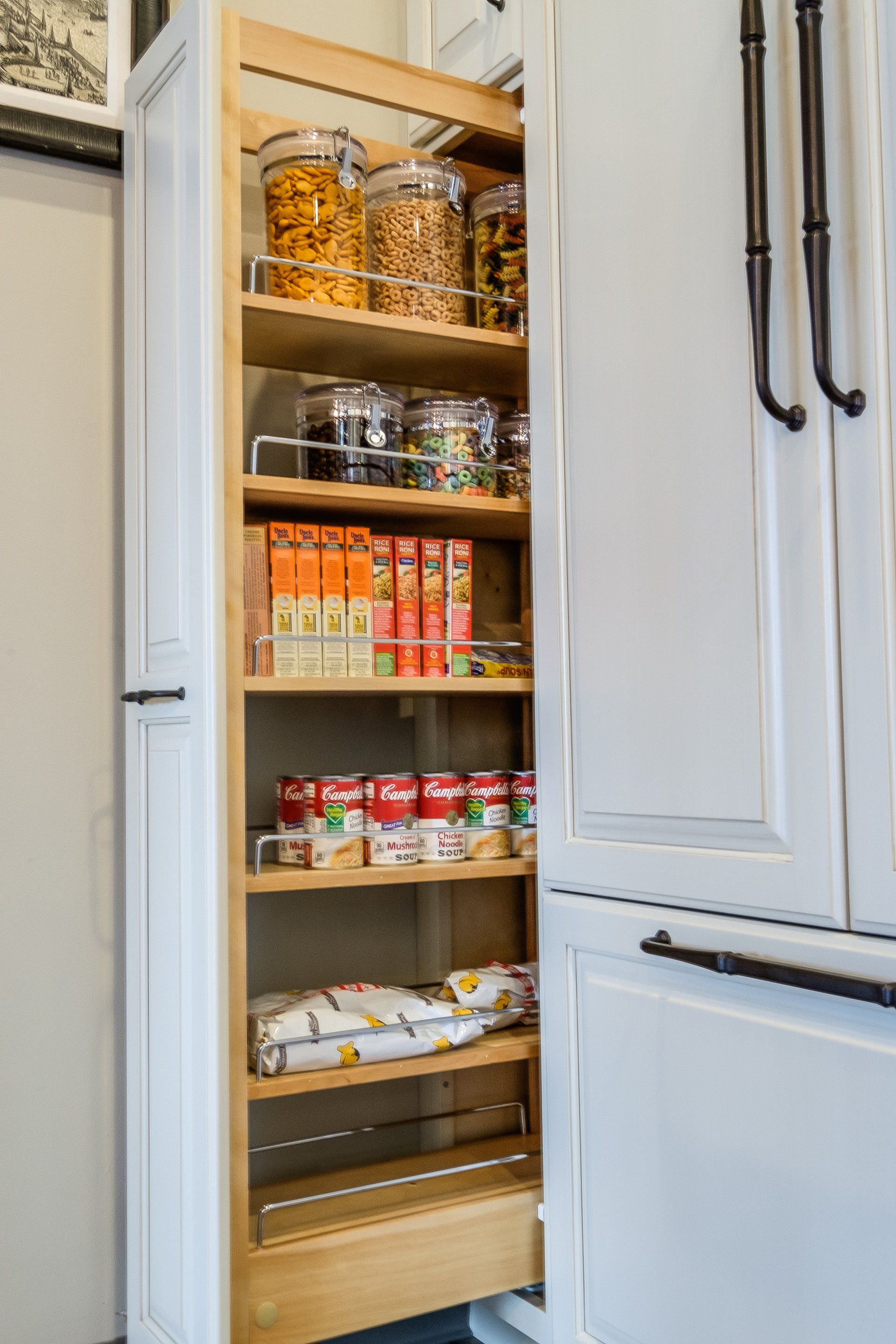 Open pantry cabinet with jars, canned goods, and pantry items on wooden pull-out shelves