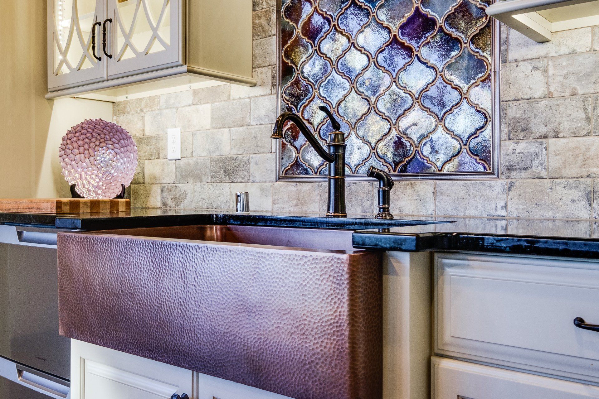Kitchen sink with dark faucet, copper apron front, stone backsplash, and diamond-pattern window