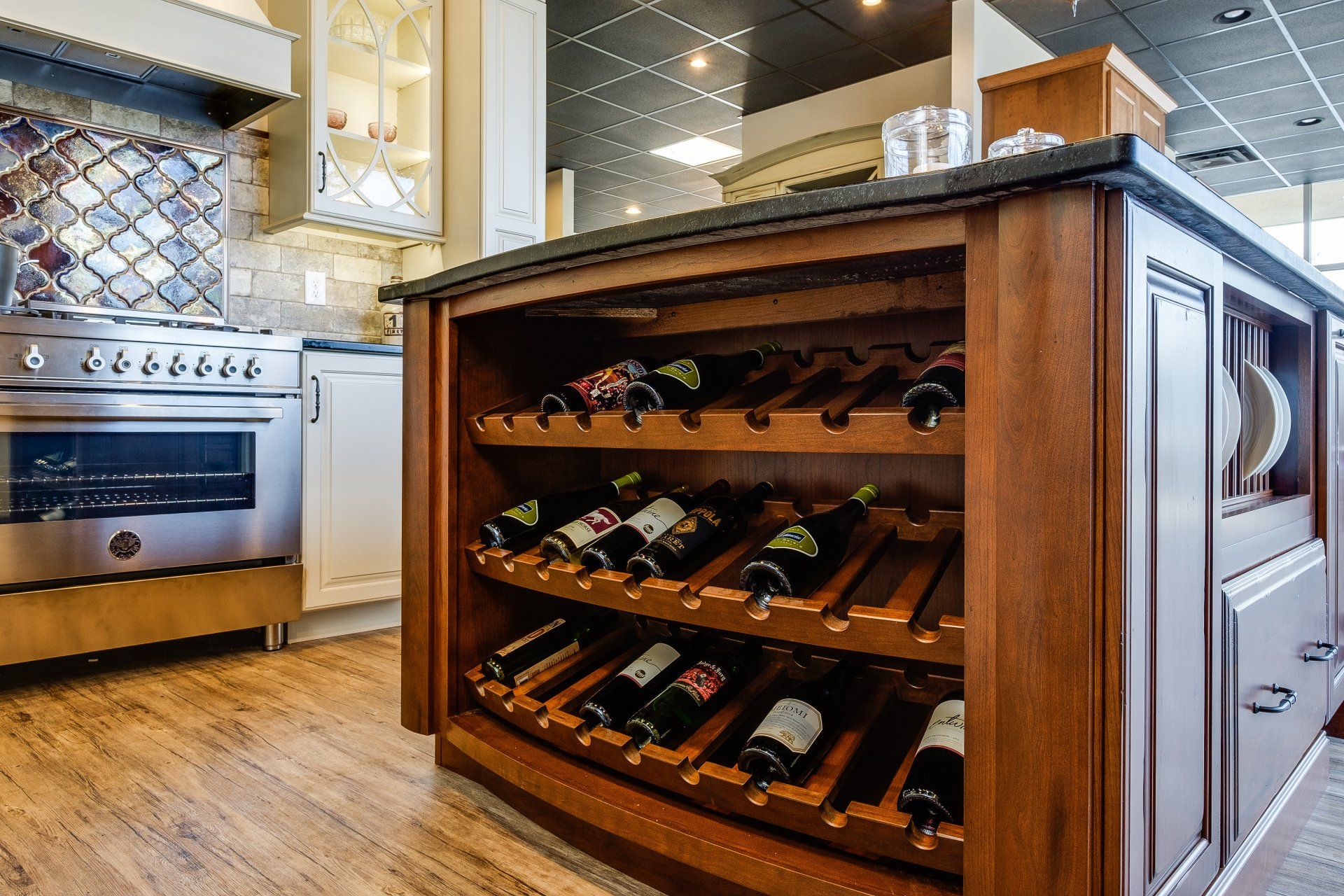 Modern kitchen island with built-in wine rack and bottles, beside a stainless steel stove and tiled backsplash
