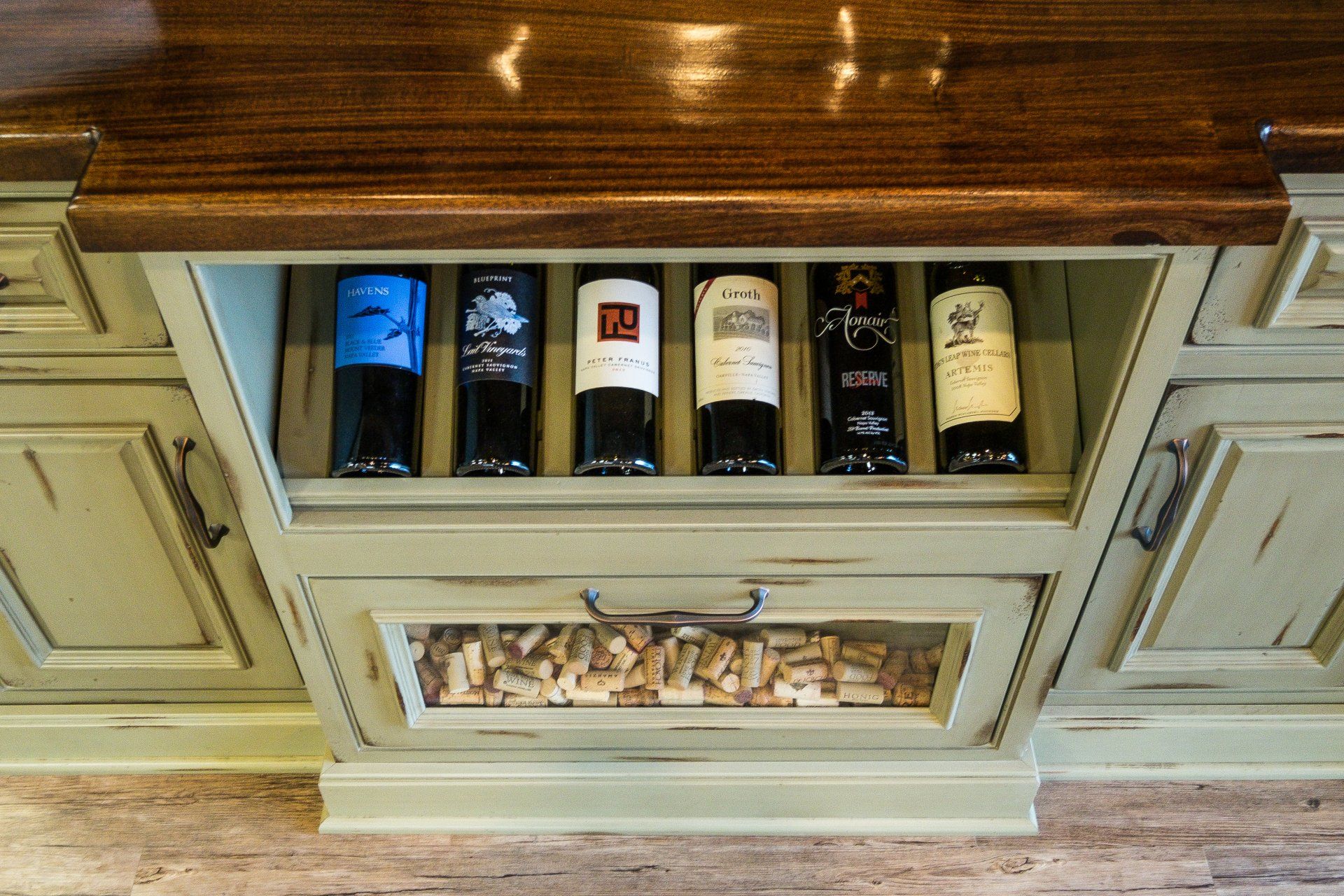 Built-in wine rack with six bottles in a cream cabinet under a wooden countertop