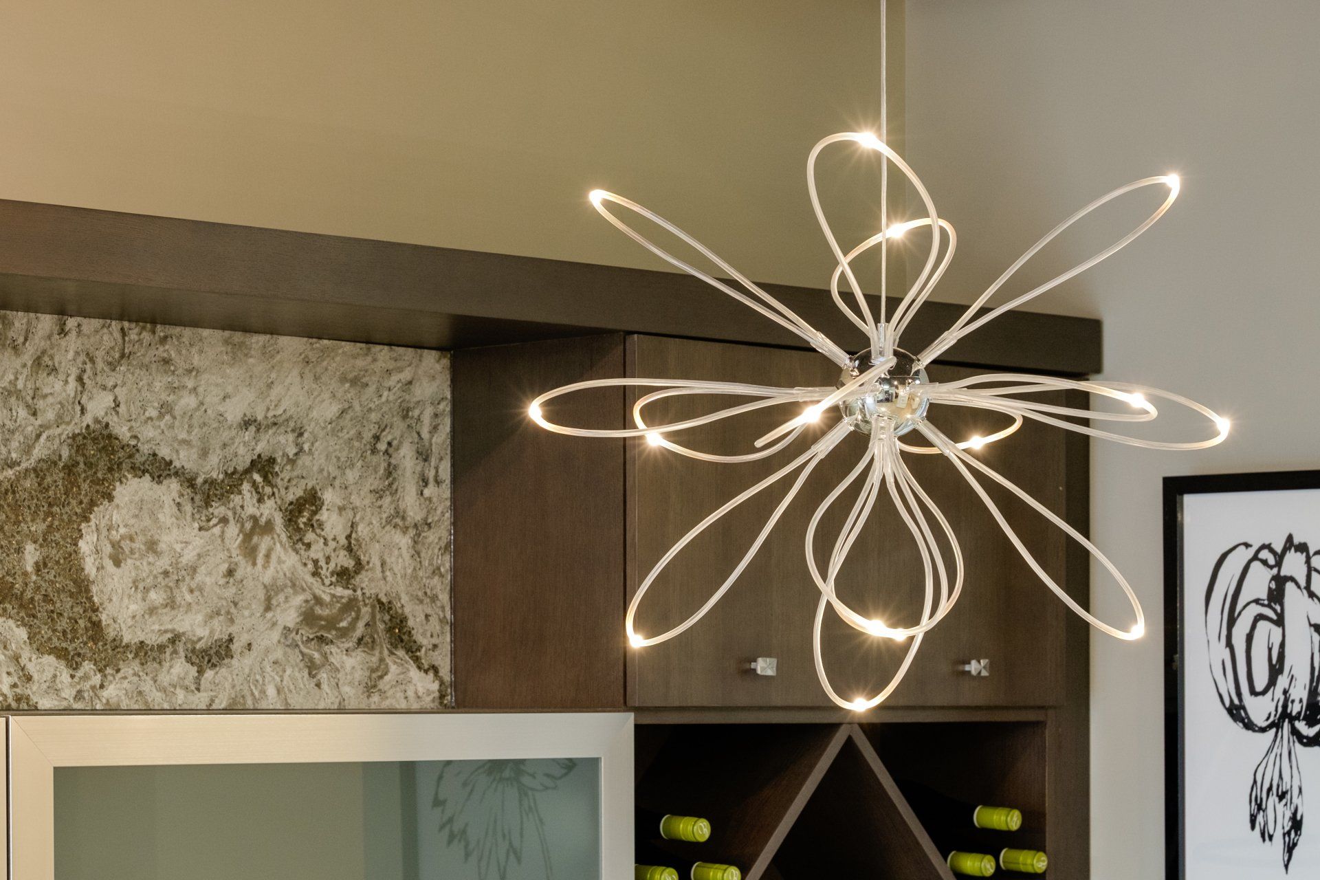 Modern floral-style chandelier glowing above a shelf and framed artwork in a contemporary room