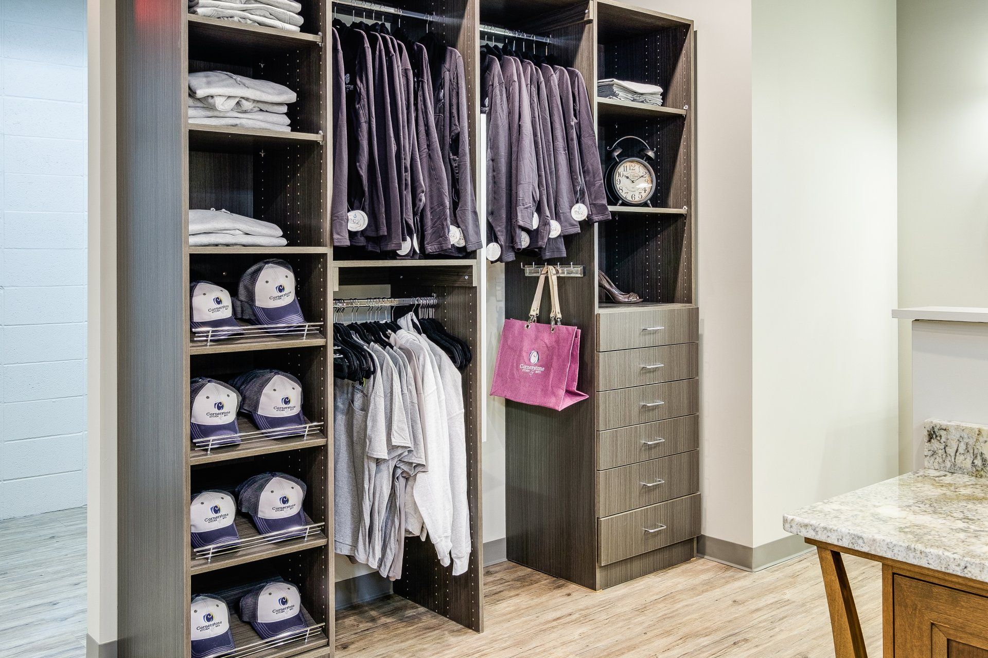 Built-in closet with shelves, hanging clothes, drawers, towels, and a pink handbag in a bedroom.